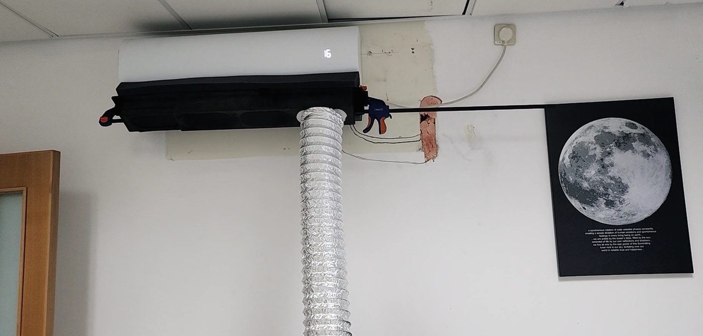 Prototype of the add-on mounted on a wall AC unit, with a flexible duct carrying the air away